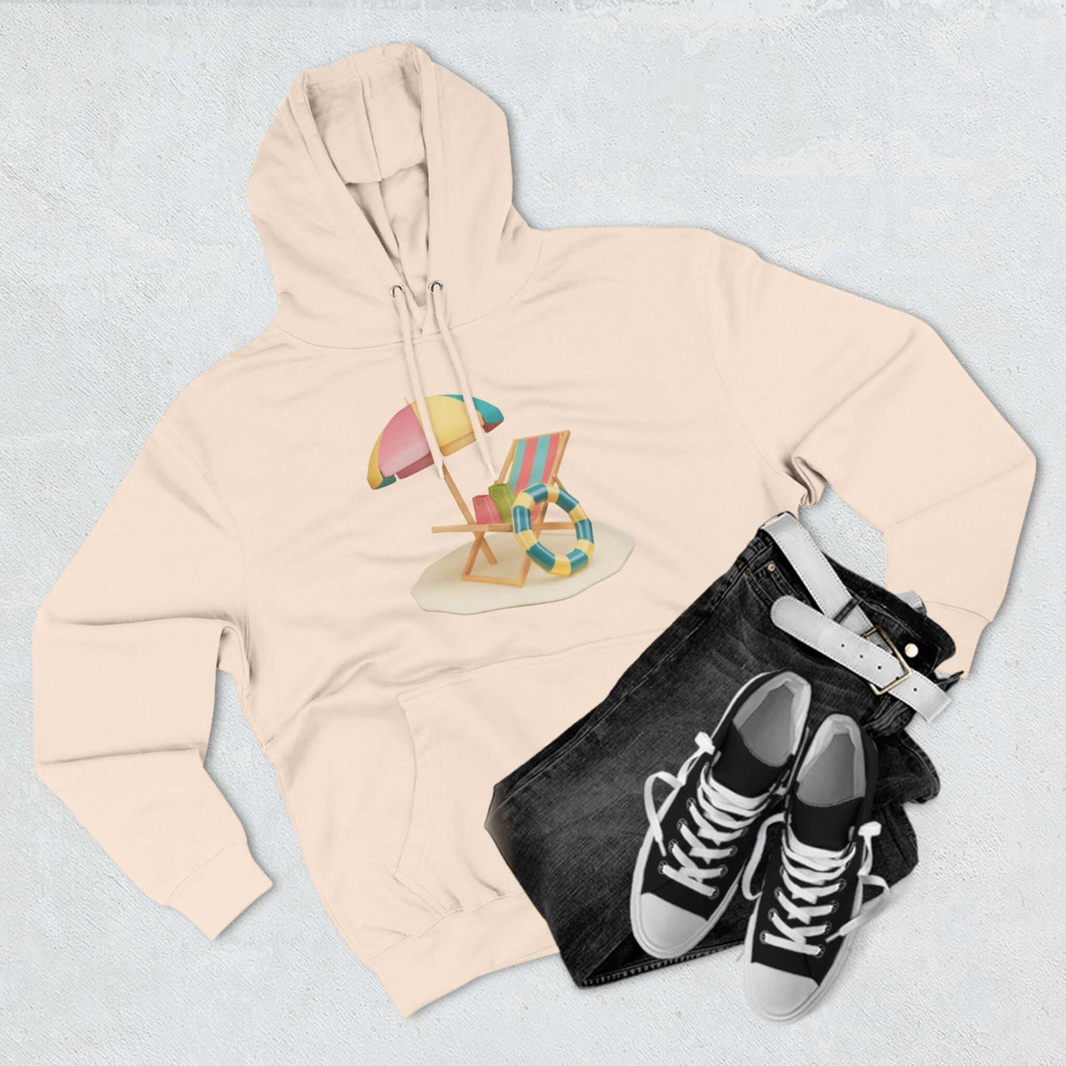 Cozy cream hoodie with beach chair and umbrella design, paired with black jeans and sneakers. Perfect for casual wear.